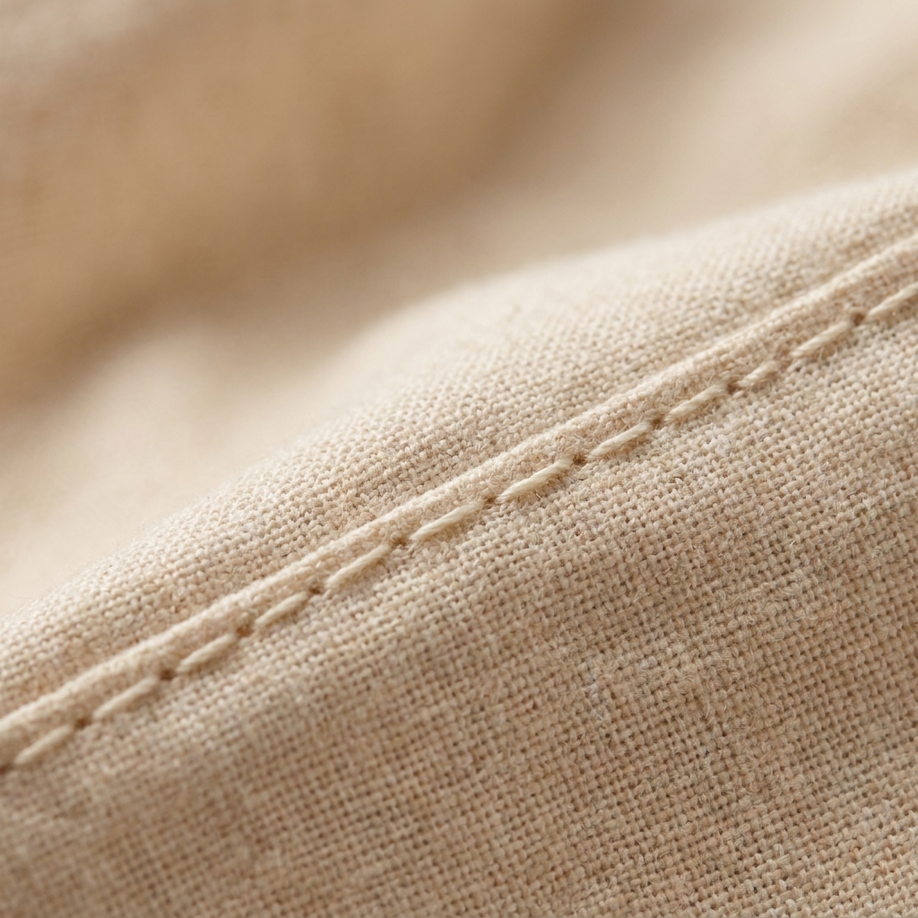 A close-up photograph of a straight stitch seam on woven cotton fabric showing neat, even stitches on the top side