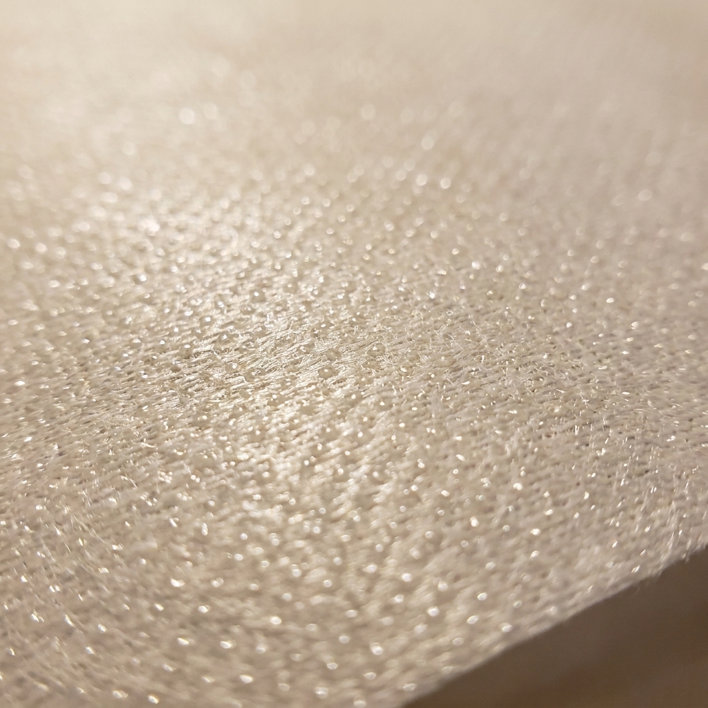 A macro-style close-up photo of fusible interfacing showing the tiny adhesive dots on the shiny glue side